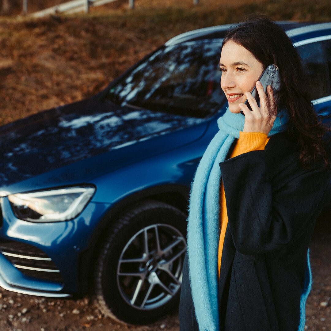 A woman standing in front of her Mercedes SUV, talking on a smartphone.