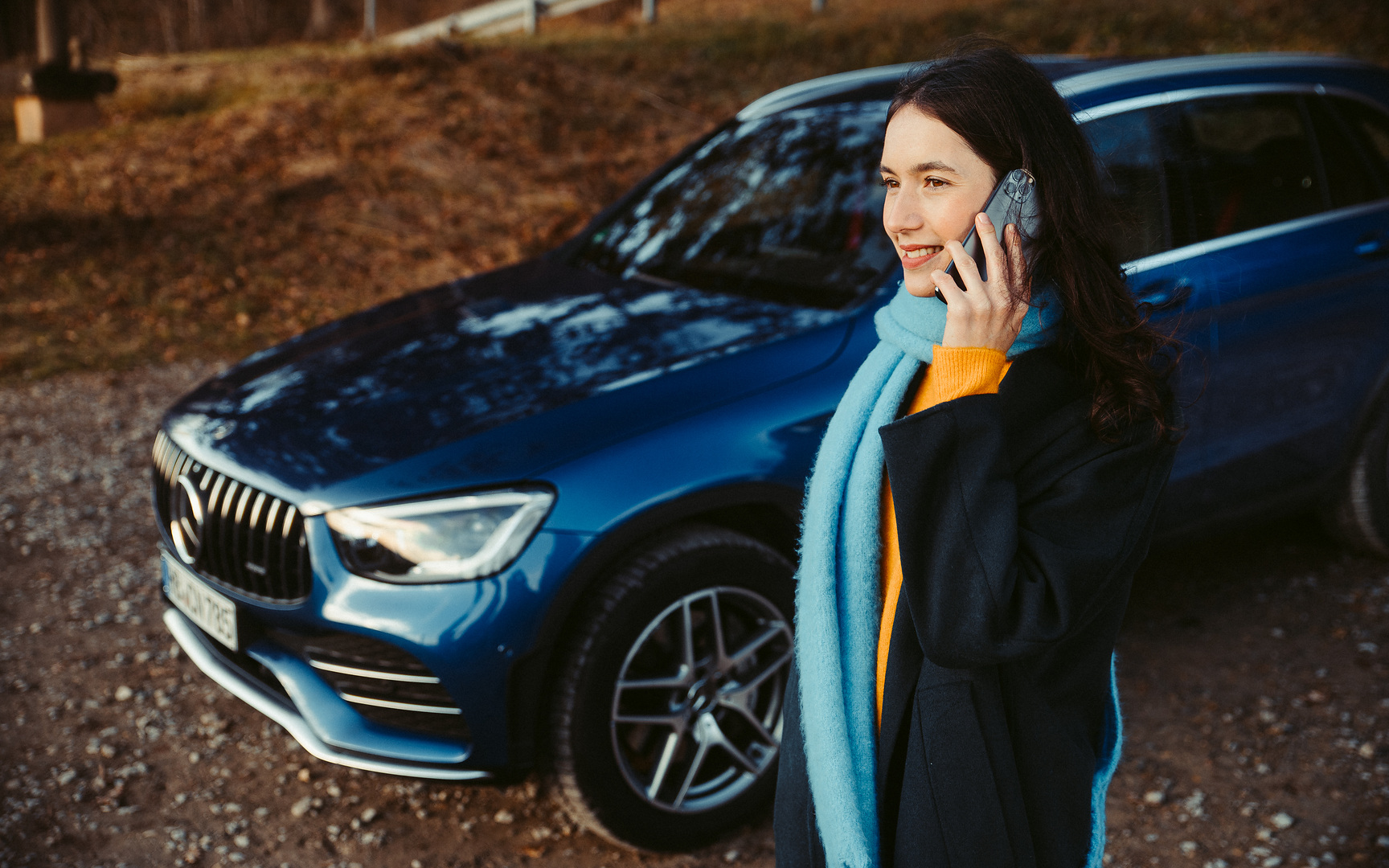 Roadside Assistance | Mercedes-Benz A woman standing in front of her Mercedes SUV, talking on a smartphone.