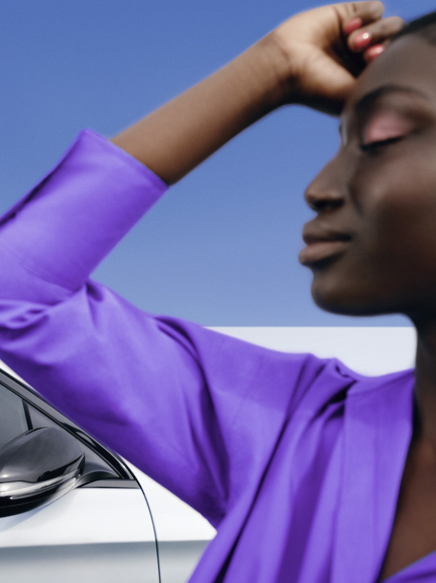 A woman standing relaxed in front of her Mercedes with an emotionless facial expression.