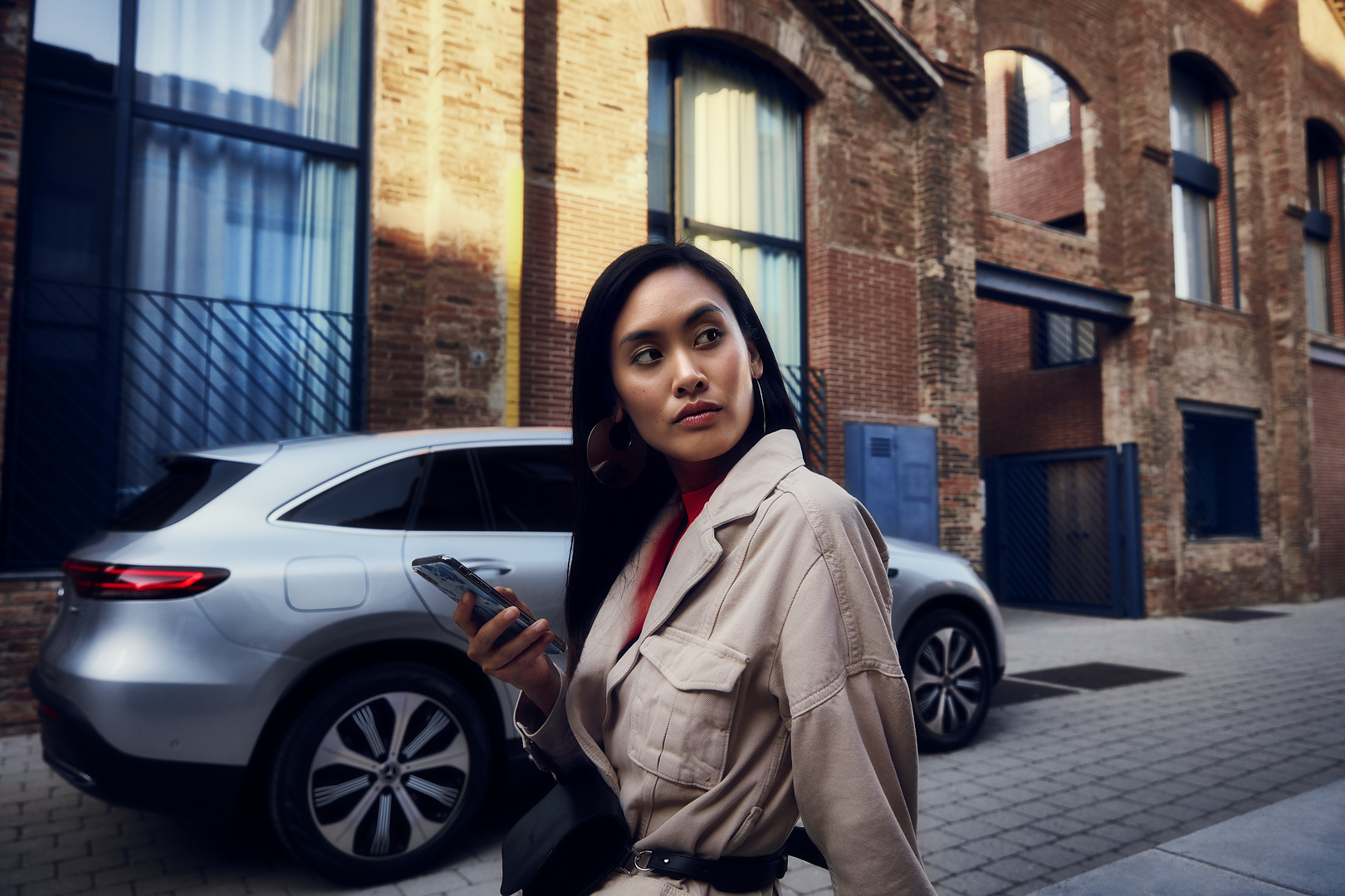 Online appointment booking | Mercedes-Benz A woman standing in front of her Mercedes with a smartphone in her right hand.