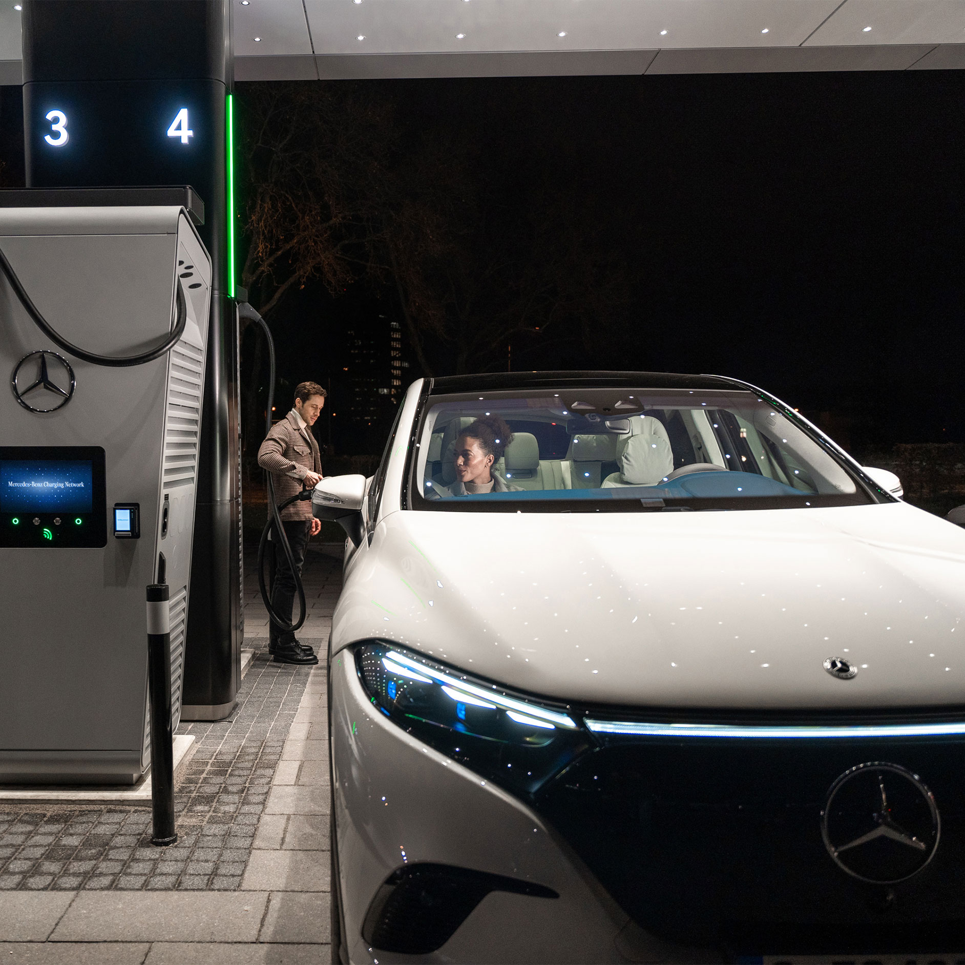 Public charging | Charging | Mercedes-Benz A person charging a Mercedes-Benz EQS SUV at a charging station.
